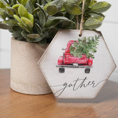 First Christmas ornament with red truck and gather written on it handing from a plant sitting on a wooden table top